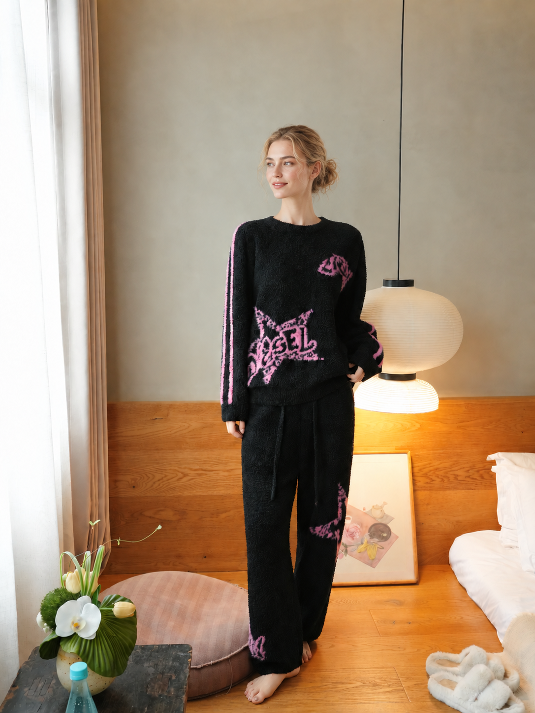 Full-body view of a woman wearing black half fleece pajamas with pink star lettering and sleeve stripes