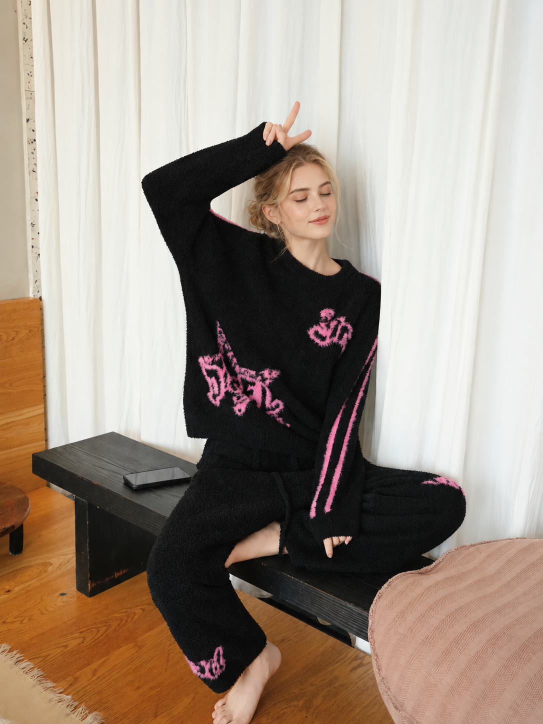 Seated woman wearing black graffiti star half fleece pajamas with pink graphics and matching pants