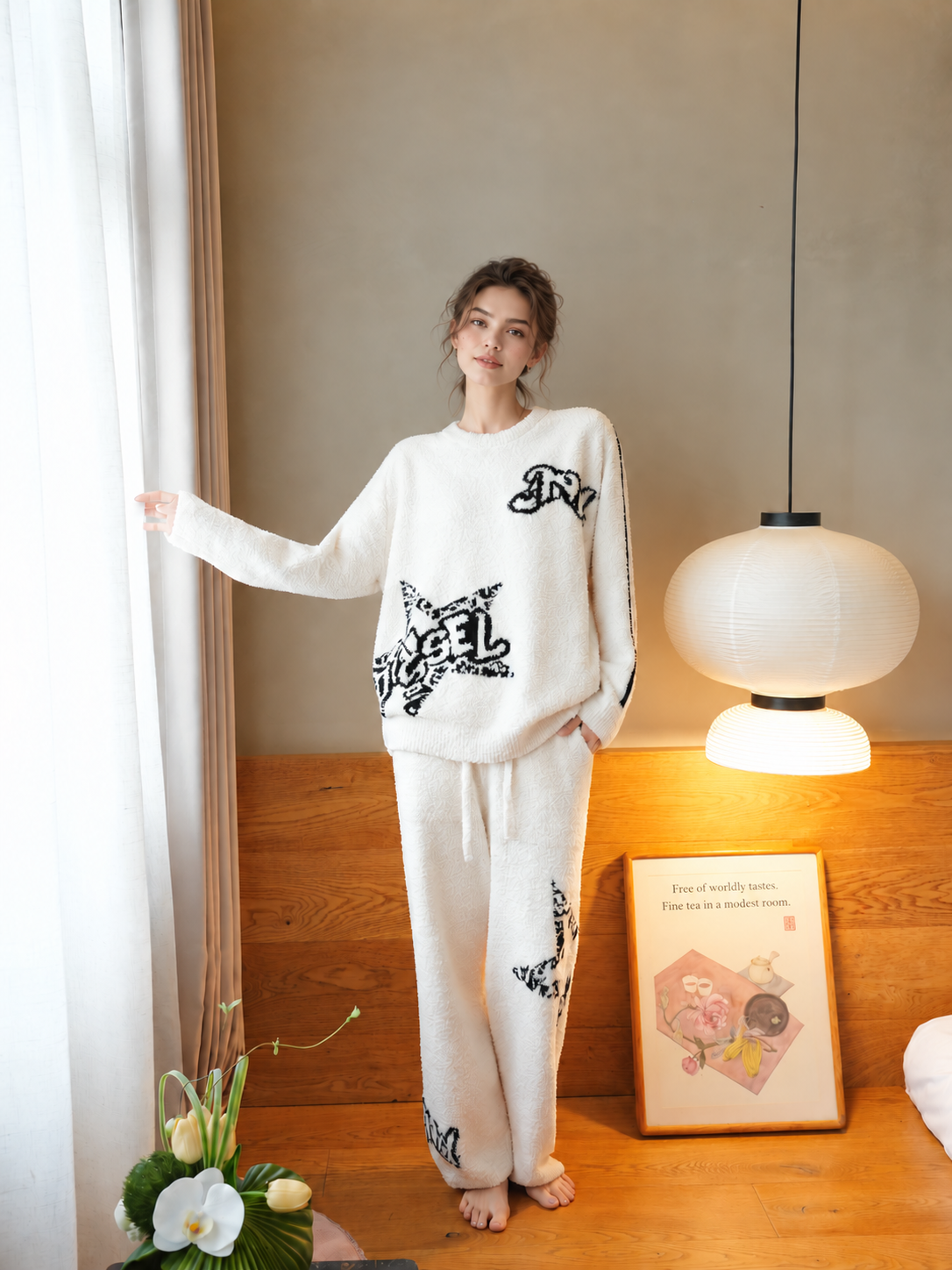 Woman standing beside a window in white graffiti star fleece pajamas with matching full-length pants