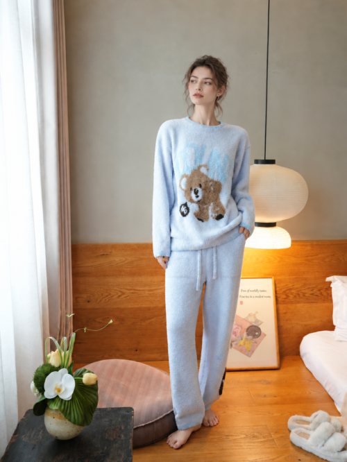 Full-body view of a woman wearing light blue teddy bear half fleece pajamas with matching drawstring pants
