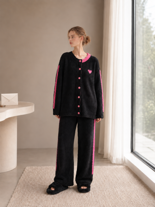 Full-body view of a woman wearing black pink heart fleece cardigan pajamas beside a window